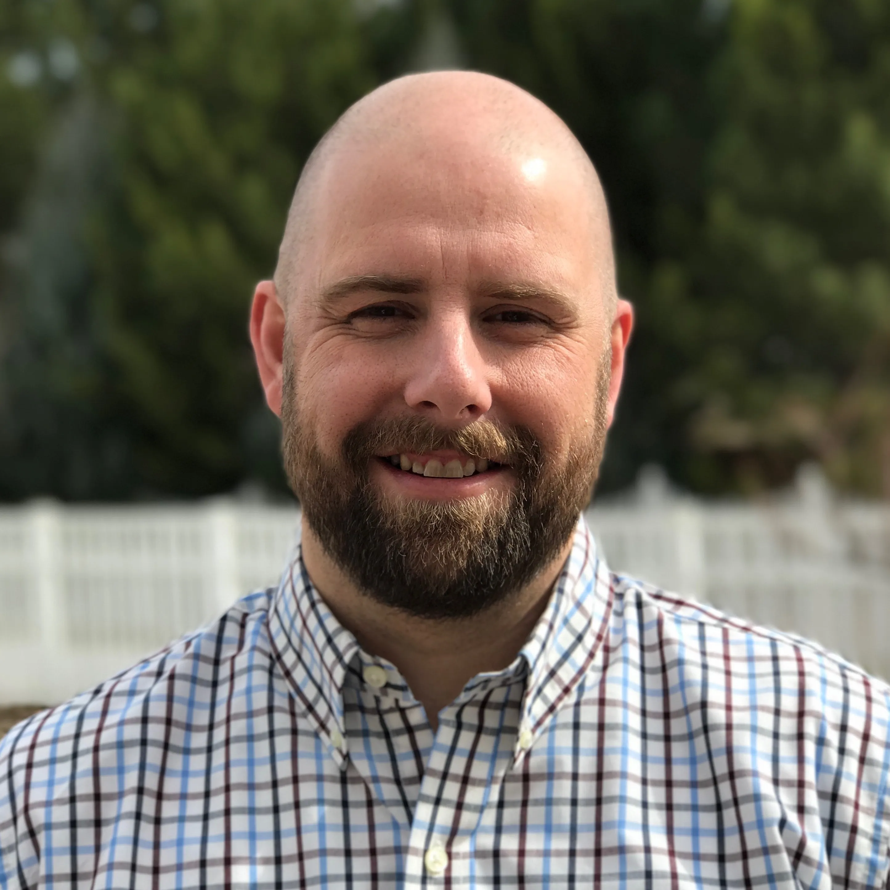 Kory Garner — smiling outdoors in a checked button-down
